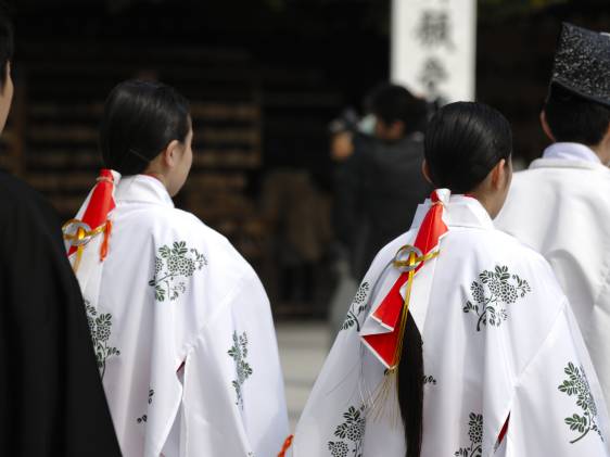 Two shrine maidens seen from behind, with long hair and white robes